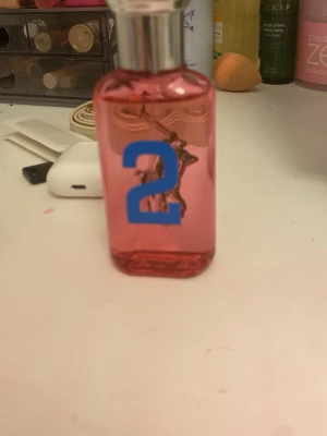 Ralph Lauren Big Pony 2 parfym - Säljer en parfym från Ralph Lauren Big Pony Collection, nummer 2. Flaskan är rosa med blå och lila siffror samt grönt polospelmotiv. Snygg och färgstark design med silverfärgad kork. Perfekt för dig som gillar sportiga och fräscha dofter.