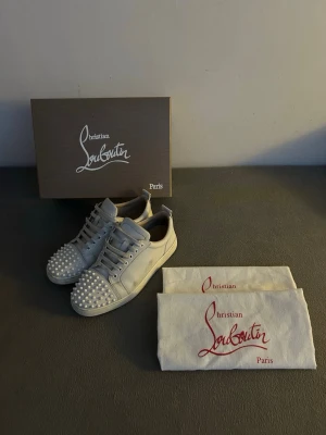 Vita Loubs (lägg bud) - Säljer ett par vita Loubs. Skorna har klassisk låg profil, vita skosnören och är tillverkade i läder. Kommer med originalkartong och dustbags.  De har en liten defekt på sidan av ena skon och saknar 1 spik. Men det syns inte om man inte kollar nära. Perfekta för dig som vill sticka ut med exklusiv stil. Tveka inte på att skriva om frågor!
