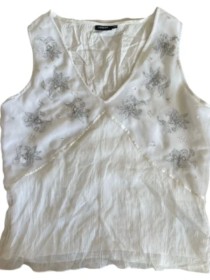 Meshlinne från äldre Lindex - Vitt mesh v-ringad blommigt meshtopp med silvriga blombroderier och detaljer 🤍pytteliten skråma (se sista bild) Jag brukar ha strl XS-S i toppar för referens!