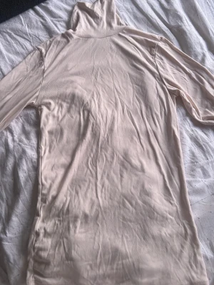 Beige polotröja i mjukt material - Långärmad beige polotröja i ett mjukt och stretchigt material. Tröjan har en hög polokrage och en smal passform som sitter snyggt på kroppen. Perfekt att styla lager på lager eller bära som den är.