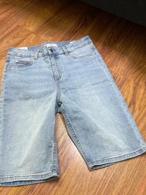 Ljusblå denimshorts från Zane - Ljusblå denimshorts från Zane med klassisk femficksdesign och raka ben. Shortsen har gylf med dragkedja och knapp, samt bakfickor. Tillverkade i mjukt jeansmaterial som ger en avslappnad look.