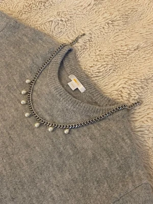 Silverfärgat halsband med pärlor - Snyggt halsband i silverfärgad metall med kedja och sju hängande vita pärlor. Perfekt för att ge din outfit en trendig och elegant touch. Kedjan har en klassisk design och pärlorna ger en stilren kontrast.