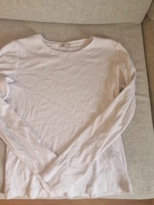 Vit ribbad långärmad topp - En basic vit ribbad långärmad topp från Cubus! Toppen har rund halsringning och är tillverkad i ett mjukt, stretchigt material som sitter skönt mot kroppen. Perfekt att styla med jeans eller kjol för en clean look! 😊