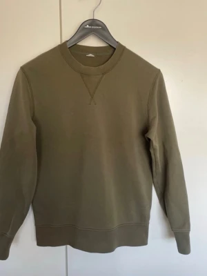 Olivgrön sweatshirt med rund hals Arket - En stilren olivgrön Arket sweatshirt med rund halsringning och ribbade muddar. Tröjan har en klassisk passform och är tillverkad i mjukt bomullsmaterial. Perfekt för en avslappnad och enkel look.
