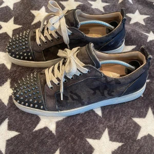 Svarta sneakers med nitar från Christian Louboutin - Intressekoll på mina Christian Louboutin klassiska röda sulor. Skorna har snörning och är tillverkade i mocka med camo detaljer. Perfekta för att ge en uppgradering i din stil 🌟