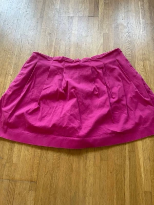 Rosa kortkjol med innbyggda shorts - En snygg rosa kortkjol med veck framtill och bak. Kjolen har en enkel design och stängs med dragkedja bak. Perfekt för dig som vill ha en färgstark, praktisk och stilren kjol till din garderob. Med innbyggda shorts och fickor. 