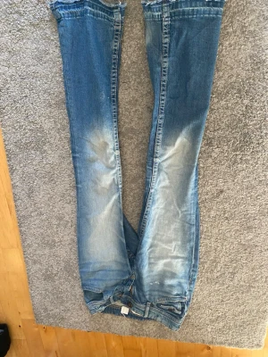 Ljusblå slitna jeans med tvättade detaljer - Säljer ett par ljusblå jeans med snygga slitningar och tvättade detaljer på benen. Jeansen har klassisk femficksmodell och raka ben. Perfekta för en avslappnad och trendig look. Materialet är bomullsdenim.