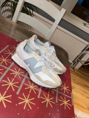 New Balance vita och beige sneakers - Snygga sneakers från New Balance i vitt och beige med grå detaljer. Skorna har en låg siluett, klassisk snörning och ovandel i en mix av mocka och textil. Perfekta för en stilren och sportig look.