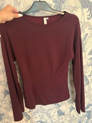 Formad topp Nelly - En stilren mörkröd långärmad topp med rund halsringning. Modellen är figurnära och passar perfekt till jeans eller kjol. Enkel design utan mönster eller detaljer, vilket gör den lätt att matcha.
