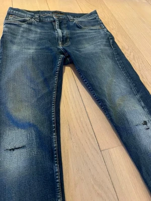 Mörkblå skinny jeans med slitningar - Snygga mörkblå skinny jeans med slitningar på knäna och lätt tvättad look. Klassisk femficksmodell med dragkedja och knapp. Jeansen har en smal passform och är tillverkade i stretchigt denimtyg för extra komfort.