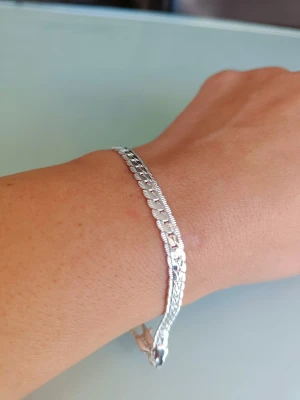 Snyggt silverfärgat armband - Stilrent armband i silverfärg med platt, glänsande kedja och diskret mönster. Armbandet har ett klassiskt karbinlås och passar perfekt för dig som gillar enkel men elegant design. Materialet är metall med silvrig finish.