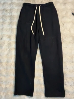 Svarta mjukisbyxor ArtieMaster M - Svarta mjukisbyxor från Art The Master Streetwear Collection med raka ben, elastisk midja och vita dragsnören. Byxorna har sidofickor och är tillverkade i ett mjukt material som passar perfekt för en avslappnad stil.