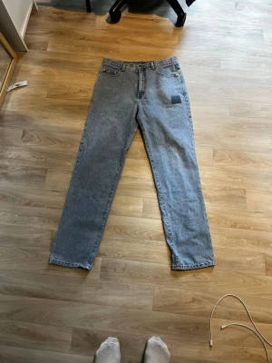 Ljusblå raka jeans från Guess. Vi kan förhandla - Säljer ett par klassiska ljusblå jeans från Guess med rak passform och hög midja. Jeansen är tillverkade i 100% bomull och har fem fickor samt en patchdetalj på ena benet. Perfekta för en avslappnad och tidlös stil.