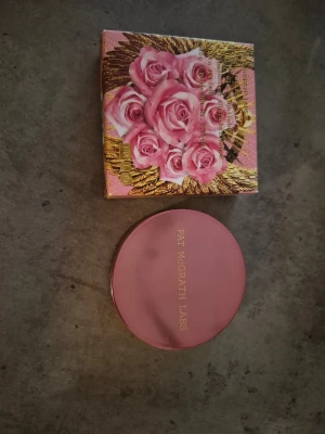 Pat McGrath Labs highlighter rosa - Highlighter från Pat McGrath Labs i en lyxig rund rosa dosa med spegel. Kommer i en vacker ask dekorerad med rosa rosor och guldiga detaljer. Färgen är en mjuk, ljusrosa nyans som ger glow till huden. Testad/swachad! Fin produkt! Lyxig förpackning.