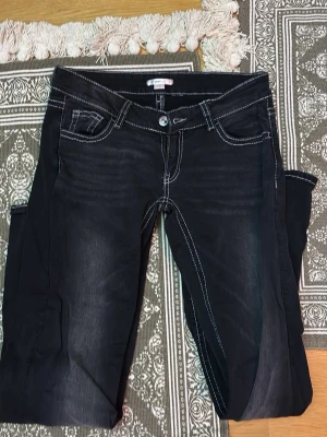 Svarta jeans från Gina Tricot - Snygga svarta jeans från Gina Tricot med kontrasterande vita sömmar och klassisk femficksmodell. Jeansen har en rak passform och är tillverkade i ett stretchigt denimtyg som ger en bekväm känsla. Perfekta för en trendig och avslappnad stil.