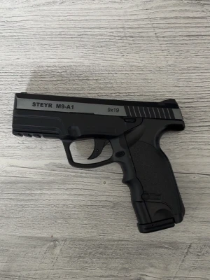 Svart Airsoft Steyr M9-A1 - Säljer en svart Airsoft Steyr M9-A1 i plast och metall med detaljerad design. Pistolen har räfflad greppyta och tydliga märkningar på sidan. Kaliber .177 (4,5mm BB) och 9x19 står på vapnet. Perfekt för samlare eller luftvapenentusiaster. PRIS KAN DISKUTERAS!!!!