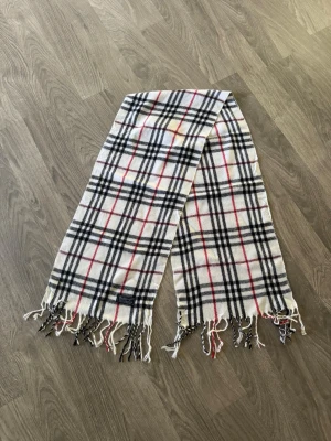 Burberry scarf - Vit burberry scarf,  tillverkad i mjuk ull och perfekt för att hålla värmen under kyliga dagar. Snygg accessoar som lyfter din outfit.