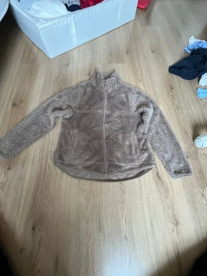 Beige teddyjacka med dragkedja - Mysig beige teddyjacka med hel dragkedja framtill och hög krage. Jackan har långa ärmar och två sidofickor. Perfekt för att hålla värmen under kyliga dagar. Tillverkad i fluffigt teddy-material som känns supermjukt. Liten fläck på armen💞