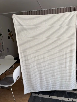 Vit ribbad filt i mjukt tyg - Stor vit filt med ribbad struktur, tillverkad i mjukt tyg. Perfekt att ha i soffan eller sängen för extra mysfaktor. Rektangulär form och neutral färg som passar in i de flesta hem.