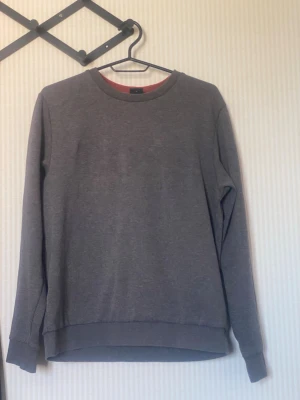 Boss Mörkgrå basic sweatshirt - En stilren mörkgrå sweatshirt med rund hals och långa ärmar. Tröjan har ribbade muddar vid ärmslut och nederkant, perfekt för en avslappnad och enkel look. Tillverkad i mjukt material som känns skönt mot huden.