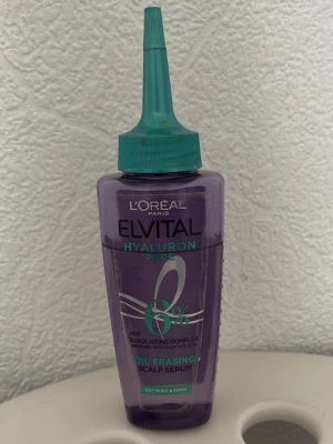 L'Oréal Elvital Hyaluron Pure Serum - Lila oljeraderande scalp serum från L'Oréal Elvital Hyaluron Pure med exfolierande komplex och 6% hyaluronsyra. Kommer i en plastflaska med turkos spetsapplikator, perfekt för fet hårbotten och rötter.