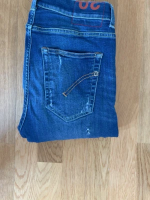 Dondup jeans w30 - Säljer ett par blå jeans med slitningar och tvättade detaljer. Jeansen har raka ben, klassiska fickor och kontrastsömmar. Perfekta för en avslappnad och trendig look. Materialet är denim med stretch för extra komfort.