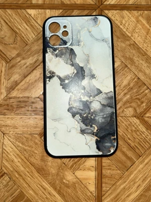Mobilskal med marmormönster iPhone 11 - Snyggt mobilskal med marmormönster i svart, grått och vitt med inslag av guld. Skalets kanter är svarta och det är gjort i ett tåligt plastmaterial. Passar till iPhone 11 och är använd ett bra tag, men bra skick! Perfekt för dig som vill ha en stilren look på mobilen.