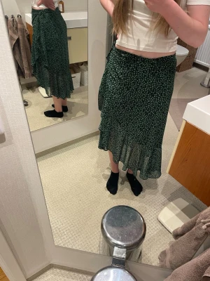 Grön blommig omlottkjol från Bershka - Snygg grön omlottkjol från Bershka med små blommor i ljusgrönt. Kjolen har volangkant nertill och är tillverkad i ett lätt, flowy material. Perfekt för dig som gillar en feminin och trendig stil.