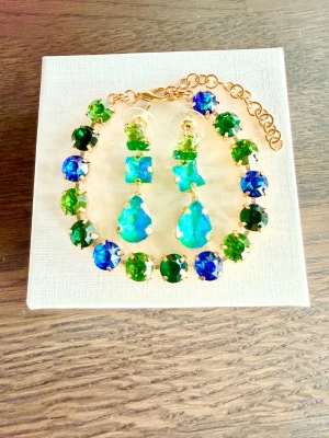 Smyckeset blå och gröna stenar - Snyggt smyckeset med blå och gröna glittrande stenar infattade i guldfärgad metall. Armbandet har 8mm stora stenar i peridot, emerald och Bermuda blue (skimrar i blå/grön). Det har justerbar kedja och ger en färgstark och lyxig känsla. Örhänge med matchande stenar, längd 3,8cm. Perfekt för dig som vill sticka ut med accessoarer i coola färger.