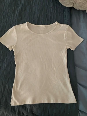 Ribbad vit t-shirt med rund hals - En stilren vit ribbad t-shirt med rund halsringning och korta ärmar. Perfekt basplagg som passar till det mesta och har en smickrande passform. Enkel och snygg design som är lätt att matcha.