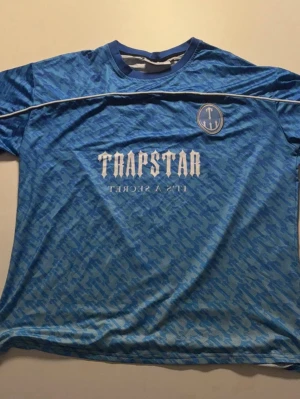 Fotbolls tröja  - En fin blå tröja en logotyp av ett stort T med en text på magen och ett nummer på ryggen, helt nytt skick