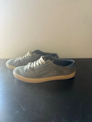Mörkblåa Saint Laurent sneakers mocka - Mörkblåa sneakers från Saint Laurent i mjuk mocka med vita snören och beige sula. Klassisk låg modell med rund tå och diskret Saint Laurent-logga på sidan. Perfekta för en stilren och avslappnad look. Skorna har några defekter som kan fixas som till exempel mockan och sulan. Skriv till mig om ni har frågor. Jag går ner lite i pris under snabb affär! mvh Alonso