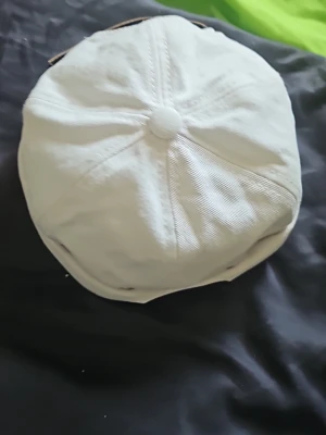 Vit keps med brunt läderband - Snygg vit keps i bomullstyg med klassisk sexpanelsdesign och knapp på toppen. Baktill finns ett justerbart brunt läderband som ger en stilren kontrast. Perfekt accessoar för en avslappnad och trendig look.