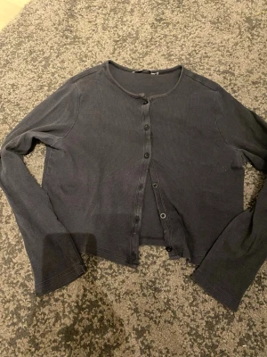 Svart ribbad kofta från 157 - Svart ribbad kofta från 157 med rund halsringning och knäppning framtill. Långärmad modell i mjukt, stretchigt material som passar perfekt till lager på lager. Enkel och stilren design som funkar till det mesta.