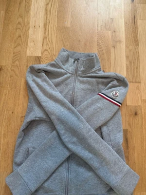 Grå ziptröja från Moncler - Grå zip hoodie från Moncler. Storlek L men sitter mer som en S/M då jag är 189 och den är lite kort men går att ha på sig. Tröjan har bra skick då den inte använts mer än 10 gånger. Är öppen på priset vid snabb affär