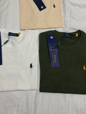 T-shirt Polo Ralph Lauren, flera färger - Klassiska t-shirts från Polo Ralph Lauren i vitt, beige och mörkgrönt. Alla har rund hals, korta ärmar och den ikoniska broderade loggan på bröstet. Tillverkade i mjuk bomull för skön känsla och stilren look.