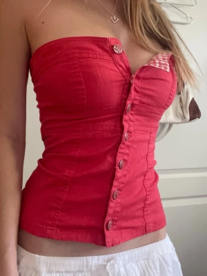 Röd vintage korsett topp  - Röd feminin korsetttopp med figurnära passform och dekorativa knappar framtill. Söt detalj med röd och vitrutigt gingham mönster som ger en fin y2k-look💗 // jättebraskick, strl S
