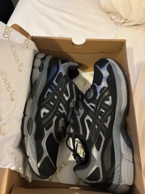 ASICS GEL-NYC svart/grå sneakers - ASICS GEL-NYC sneakers i svart och grått med coola detaljer och meshpaneler för extra ventilation. Skorna har en chunky sula och klassisk snörning. Perfekta för dig som gillar sportig och trendig stil. Ortholite-innersula för extra komfort.