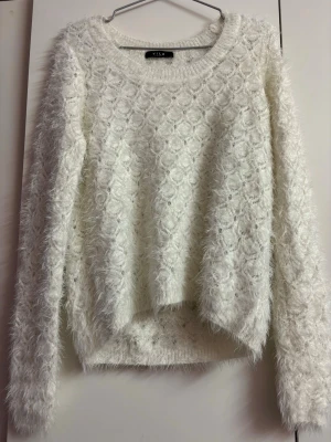 Vit fluffig stickad tröja från Vila - Supermjuk och fluffig vit stickad tröja från Vila med rund halsringning och långt ärm. Tröjan har ett diskret mönster i stickningen och ger en cozy look. Perfekt för kyliga dagar när du vill vara både varm och snygg.