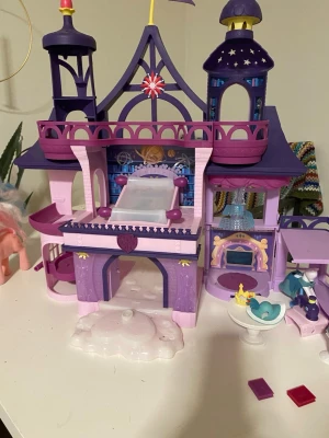 My Little Pony Twilight Sparkle Slott med tillbehör - Ett stort My Little Pony-slott med flera våningar och rum. Slottet har ljusfunktioner som lyser upp olika delar av slottet i olika färger. Det ingår även ett flertal My Little Pony-figurer i olika storlekar, inklusive några äldre, sammetsbeklädda ponnyer. Dessutom medföljer en stor låda med diverse små tillbehör som möbler, mat och andra smådelar för att inreda slottet och leka med ponnyerna.