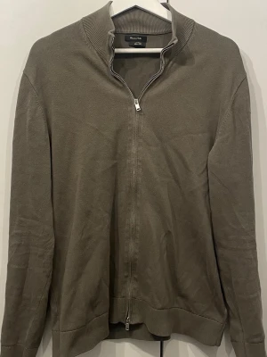 Zipkofta från Massimo Dutti - Stilren ziptröja från Massimo Dutti i 100% bomull. Tröjan har hög krage, hel dragkedja och ribbade muddar. Perfekt för lager-på-lager och enkel att matcha med olika outfits.