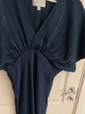 Klänning för bal/bröllop/fest - Elegant marinblå satin  långklänning från Azize med v-ringning och generösa korta ärmar. Klänningen har ett snyggt fall och markerad midja. Tillverkad i ett glansigt material som ger en lyxig känsla. ( riktig pris kostar den 2000) sänker. Och använt den 1 gång 