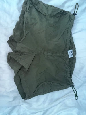 Olivgröna lågmidjade cargoshorts - Säljer ett par olivgröna shorts från urban outfitters med elastisk midja och snörning i sidorna. De har en loose passform. 