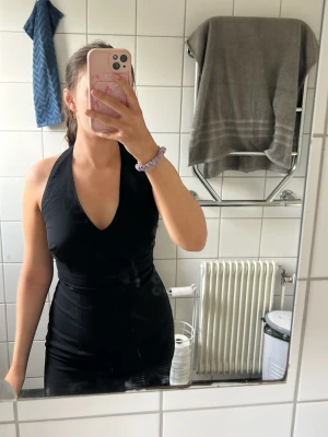 Svart linneklänning  - Snygg svart klänning med halterneck och djup v-ringning. Klänningen är figurnära och har en elegant look. Det är en linneklänning det är en lite öppning vid benet den är använd 2 gånger men super fin klänning. 
