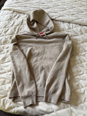 Beige hoodie från RYVLS - Mysig beige hoodie från RYVLS med huva och dragsko. Tillverkad i mjukt stickat material som känns skönt mot huden. Perfekt för chill dagar eller när du vill ha en enkel och stilren look. Långa ärmar och ribbade muddar för extra komfort.