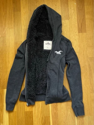 Hollister teddy/faux fur hoodie - Supermjuk Hollister hoodie i grå faux fur-material! Ger en mysig Y2K aesthetic, perfekt för kyliga kvällar. Storlek M (inte oversized, mer normal passtorm). Materialet är väldigt mjukt och fluffigt på insidan, skön mot huden. Säljes pga garderobsrensning, kan skickas snabbt!