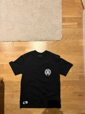 Svart Amerika  Chrome hearts T-shirt - Säljer en svart t-shirt från Chrome hearts, med vit logga och emblem tryckt på bröstfickan samt ett CH-tryck nere vid fållen. Klassisk rund hals och korta ärmar. 