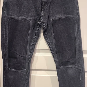 Svarta jeans från Calvin Klein Jeans med patches, w30 - Snygga svarta jeans från Calvin Klein Jeans med patches fram på lår. Klassisk femficksmodell med logga på bakfickan. Jeansen har passform ”slim fit” w30 L32 . Innerbenslängd 80 cm. Hellängd 104 cm midja 40 cm benslut 16,5cm