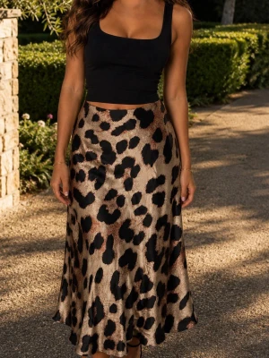 Leopardmönstrad långkjol i satin strl M  - Snygg långkjol med leopardmönster i beige, svart och bruna toner. Kjolen har en lätt glansig satinfinish och en figurnära passform som faller snyggt längs benen. Perfekt för dig som vill sticka ut med ett trendigt djurmönster.