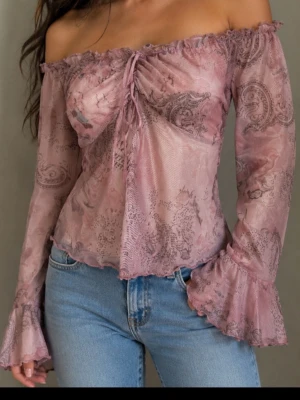 Rosa offshoulder meshblus med volang - Supersöt rosa offshoulder blus i mesh med paisleymönster och volangdetaljer vid ärmslut och hals. Blusen har snörning framtill och är transparent med långa ärmar. Perfekt för dig som vill ha en romantisk och trendig look.